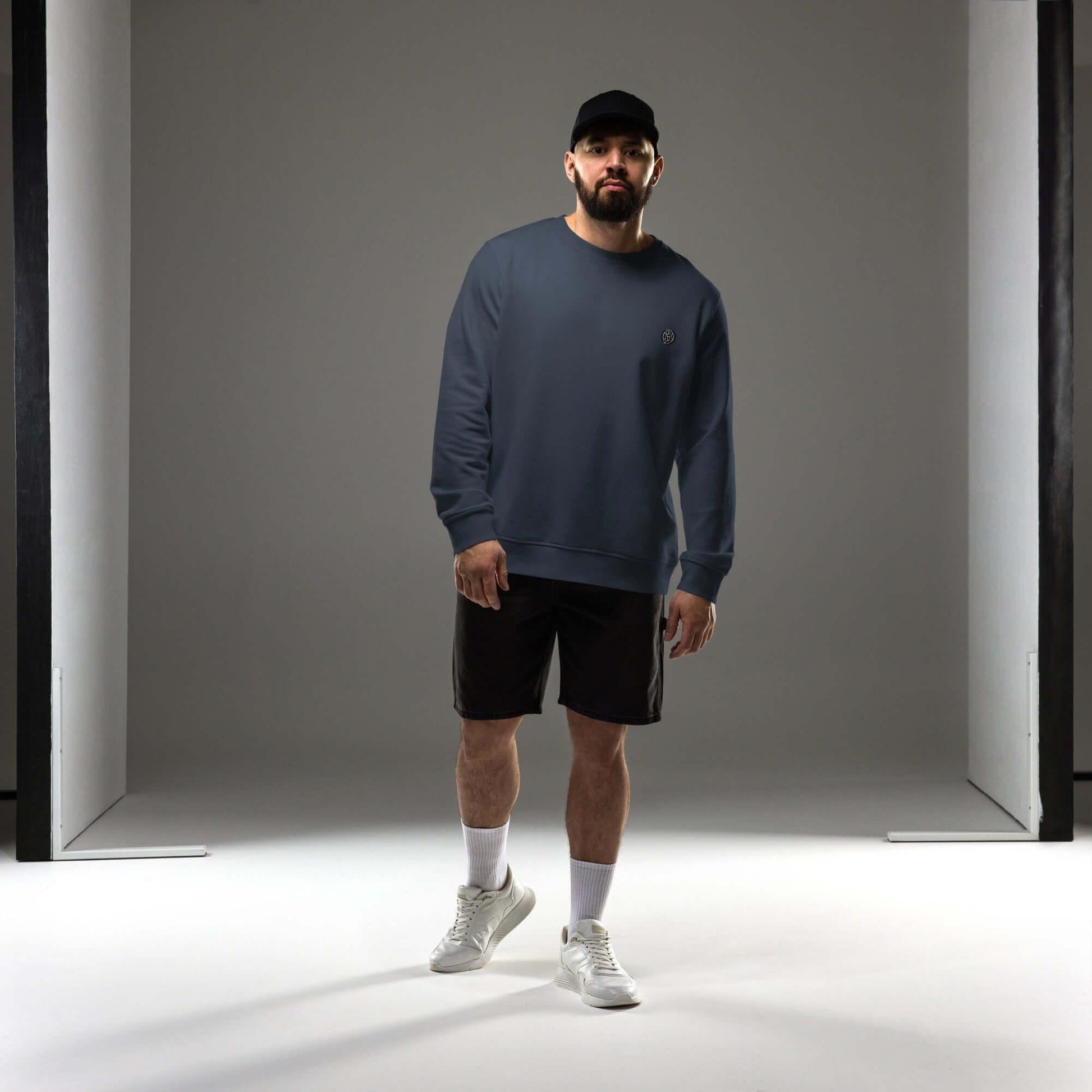 Stylish man wearing a navy Creamy Beamy Organic Sweatshirt with shorts and sneakers in a modern studio.